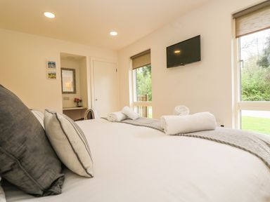 A bedroom with a made bed two rolled towels a wall-mounted tv two windows and a small desk at Elm in Truro