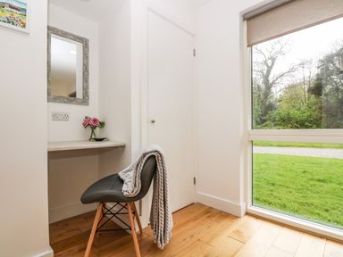 A small corner with a chair, a built-in desk, a mirror, a vase with flowers, and a large window showing greenery outside at Elm in Truro