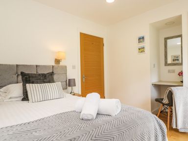 A bedroom with a bed with pillows and rolled towels on a blanket a wooden door and a small desk area with a chair and mirror at Elm in Truro
