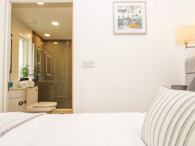 A bedroom with a bed and striped pillow facing a bathroom with a toilet shower and towels at Elm in Truro