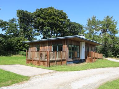 A wooden cabin with a deck and railing surrounded by grass and trees at Elm in Truro