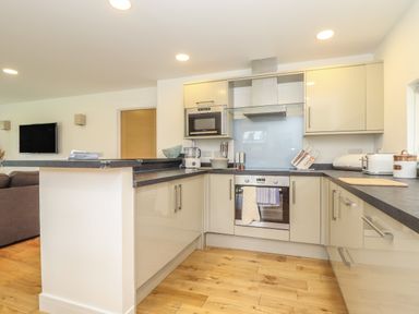 A kitchen with beige cabinets black countertops wooden floor and built in oven at Hazel in Truro