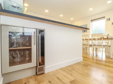 A kitchen area with a glass-fronted cabinet under a countertop and a dining table with chairs by a window at Hazel in Truro