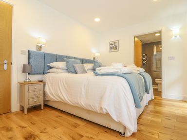 A bedroom with a large bed with blue headboard and white bedding near a wooden floor at Hazel in Truro