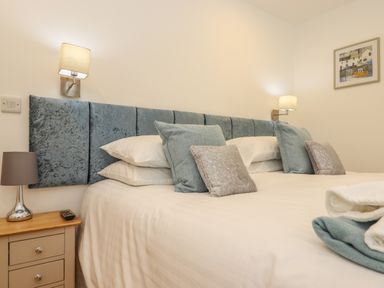 A bedroom with a blue padded headboard pillows bedside table and lamps at Hazel in Truro