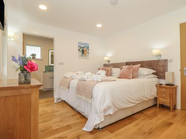 A bedroom with a double bed with pillows and rolled towels bedside tables and a dresser with flowers at Hazel in Truro