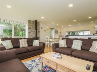 A living room with two sofas and cushions a coffee table with magazines and remote a dining table with chairs and a window showing trees at Hazel in Truro