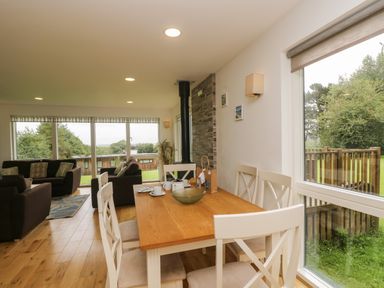 A dining table with chairs and a living room area with sofas near large windows at Hazel in Truro