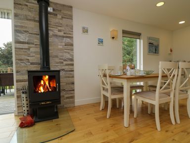 A dining area with a wooden table, white chairs, a wood-burning stove, and a glass door leading outside at Hazel in Truro