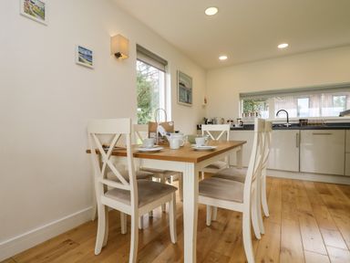 A dining area with a wooden table and four white chairs next to a kitchen with grey cabinets at Hazel in Truro