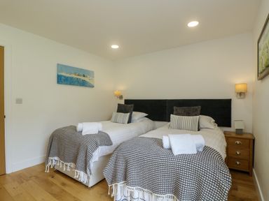 A bedroom with two single beds with blankets and pillows a wooden nightstand with a lamp two wall lamps and paintings on the walls at Hazel in Truro