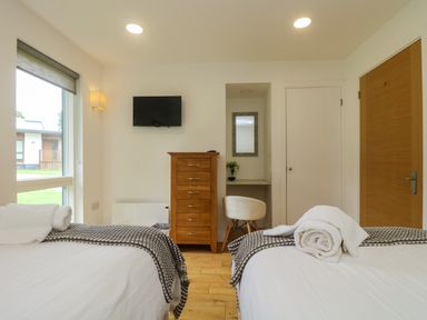A bedroom with two beds a wooden dresser a wall-mounted TV and a small desk with a chair at Hazel in Truro