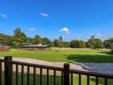 A view of a grassy area with trees and wooden buildings visible from behind a wooden railing at Juniper in Truro