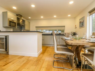 A kitchen and dining area with wooden floor a dining table with chairs and kitchen appliances at Juniper in Truro