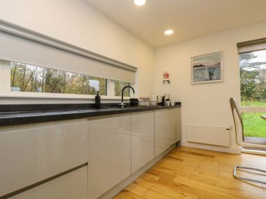 A kitchen with white cabinets black countertop a sink window above and a chair near a glass door at Juniper in Truro