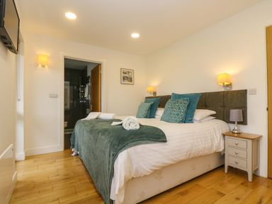 A bedroom with a double bed bedside tables wall lights and a door leading to a bathroom at Juniper in Truro