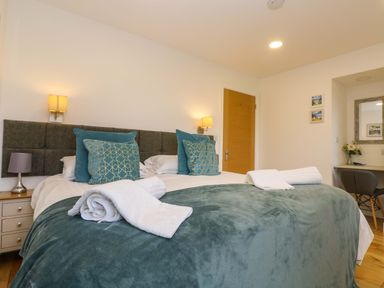 A bedroom with a bed with teal pillows and blankets and rolled white towels at Juniper in Truro