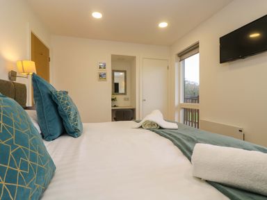 A bedroom with a bed featuring blue pillows and white towels with a window and a wall-mounted TV at Juniper in Truro