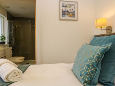 A bedroom with a bed and teal pillows next to a bathroom with a toilet and glass shower at Juniper in Truro