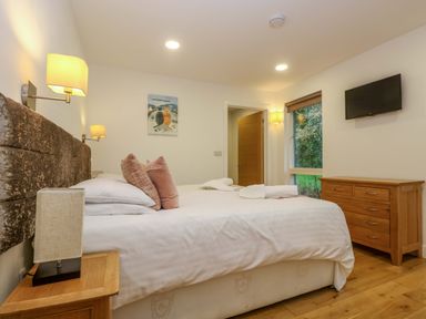 A bedroom with a bed with pillows and towels a wooden dresser a wall-mounted TV and a window at Juniper in Truro