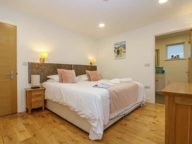 A bedroom with a double bed pink pillows bedside table and door leading to a bathroom at Juniper in Truro
