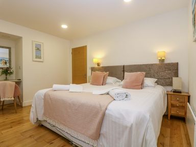 A bedroom with a large bed with pillows and folded towels bedside tables with lamps a chair with a blanket and flowers on a desk at Juniper in Truro