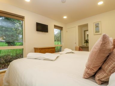 A bedroom with a bed and pillows a wooden dresser a wall-mounted TV and two large windows at Juniper in Truro