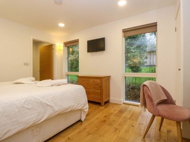A bedroom with a bed white sheets wooden dresser pink chair and two windows at Juniper in Truro
