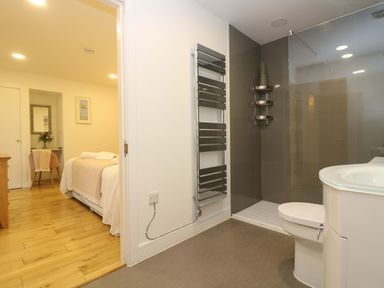 A bathroom with a toilet sink and shower next to a bedroom with a bed chair and mirror at Juniper in Truro