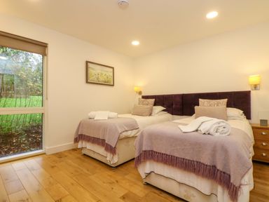 A bedroom with two single beds bedside table and window showing greenery outside at Juniper in Truro