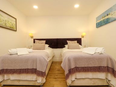 A bedroom with two single beds with blankets pillows and rolled towels on wooden floor at Juniper in Truro