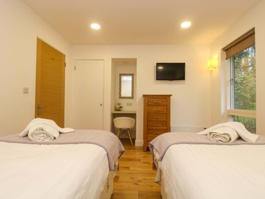 A bedroom with two single beds with folded towels a wooden dresser a wall-mounted TV a chair and desk and a window at Juniper in Truro