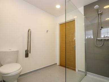 A bathroom with a toilet grab bar a wooden door and a walk in shower with a glass partition at Juniper in Truro