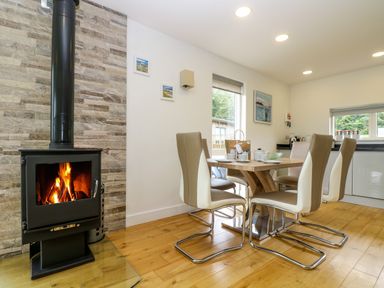 A dining area with a wooden table and six chairs near a lit wood stove at Maple in Truro