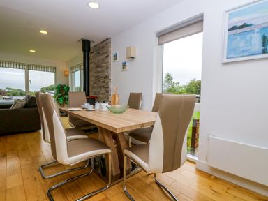 A dining area with six chairs around a wooden table next to large windows at Maple in Truro