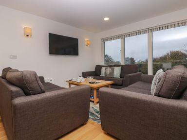 A living room with three sofas a wooden coffee table a wall-mounted television and large windows at Oak in Truro