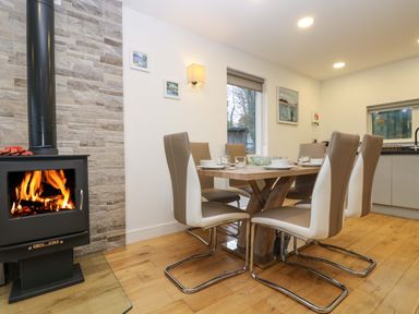 A dining area with a wooden table and six chairs near a wood-burning stove and a window at Oak in Truro