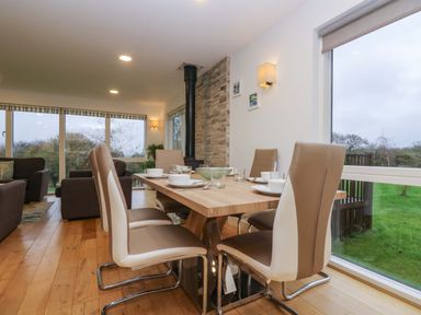A dining room with a wooden table and six chairs next to large windows showing an outdoor grassy area at Oak in Truro