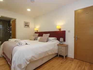 A bedroom with a double bed pillows bedside table with lamp wooden floor and a door at Oak in Truro
