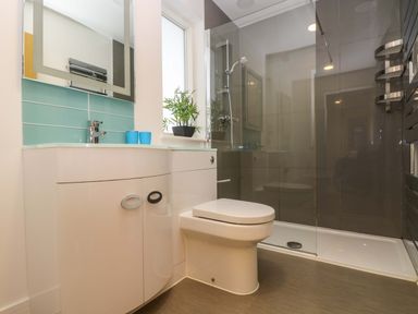 A bathroom with a white toilet a curved white vanity with a sink and a mirror above and a glass-enclosed shower at Oak in Truro