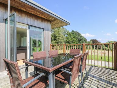 An outdoor deck with a glass table and six wicker chairs next to a wooden building at Rowan in Truro