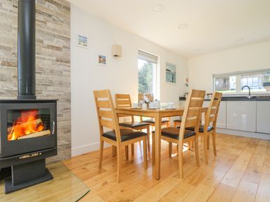 A dining area with a wooden table and six chairs next to a fireplace and kitchen at Rowan in Truro