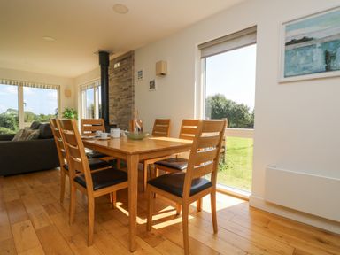 A dining area with a wooden table and six chairs next to large windows in Rowan Truro