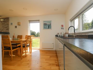 A kitchen area with wooden dining table and chairs next to a window and a countertop with a dish rack and sink at Rowan in Truro