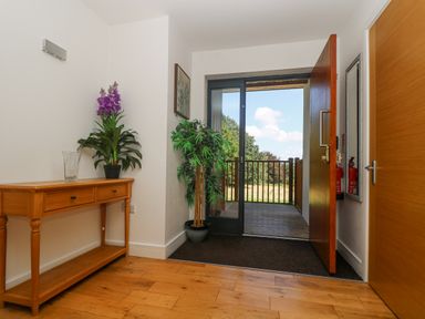 An entrance hallway with a wooden table and plants by an open door showing an outdoor deck and landscape at Rowan in Truro