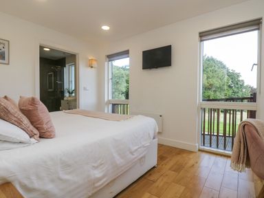 A bedroom with a bed, pink cushions, a wall-mounted TV, two windows, and a door leading to an outdoor area at Rowan in Truro
