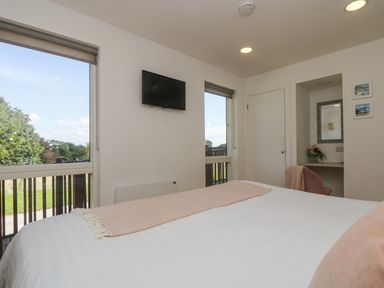 A bedroom with a bed a wall mounted TV two windows a door and a dressing table at Rowan in Truro