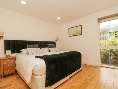 A bedroom with a large bed with black headboard and blankets wooden floor and a window at Rowan in Truro