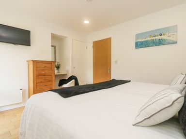 A bedroom with a bed a wooden chest of drawers a wall mounted tv and a door at Rowan in Truro