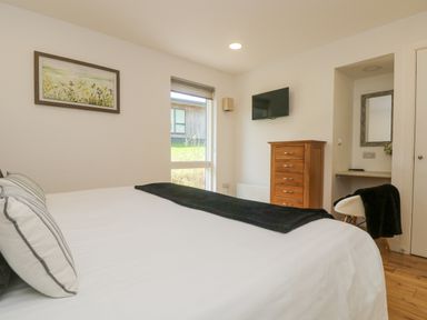 A bedroom with a bed a wooden dresser a mounted tv and a small desk with a chair at Rowan in Truro